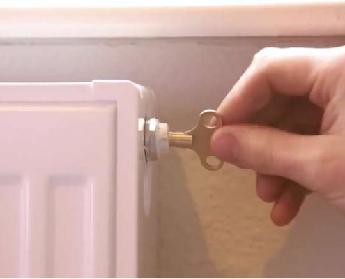 Mano utilizando la llave purgadora con un radiador convector y una pared con fondo crema