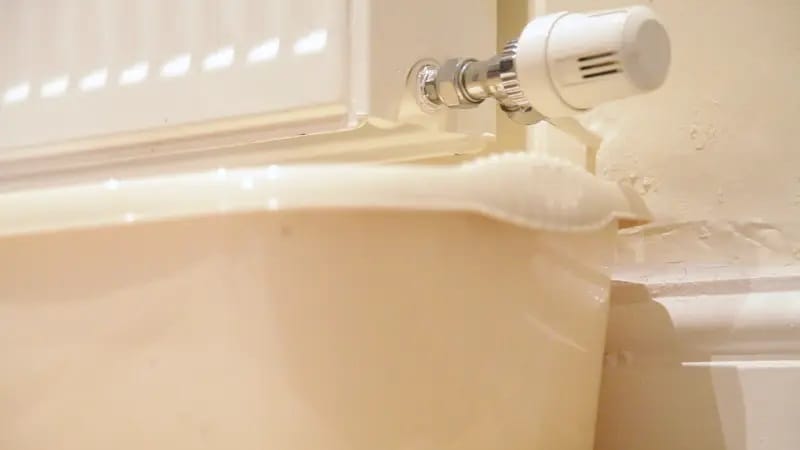 Cubo de agua para recoger goteos al vaciar un radiador con llave termostática blanca