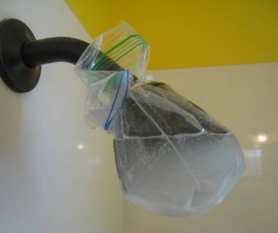 Alcachofa de ducha llena de cal siendo limpiada con vinagre blanco en una bolsa de plástico Solución para limpiar un cabezal de ducha lleno de cal con limpieza de vinagre blanco