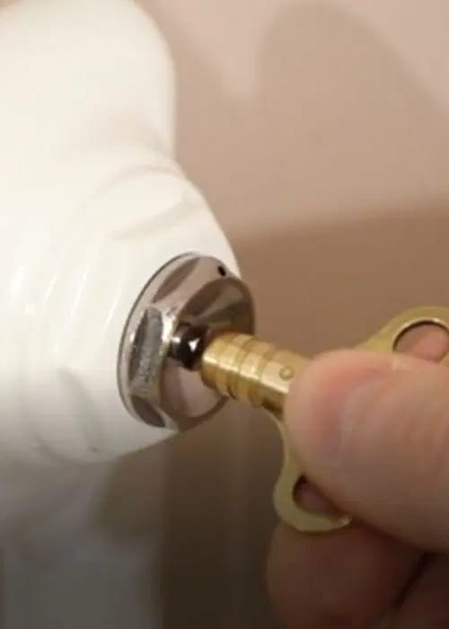 Hombre vaciando el aire de un radiador hidráulico con una llave purgadora