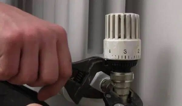 Llave de radiador termostática con cabezal blanco siendo ajustada con una llave inglesa