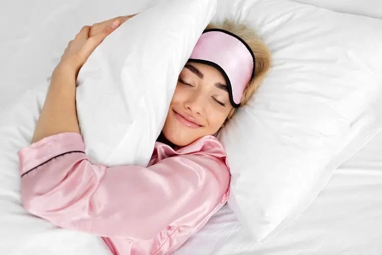 : Mujer con pijama de seda rosa durmiendo en cama con sábanas blancas